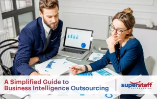 An image showing two data experts discussing graphs. The title of the blog "Decoding Data Excellence: A Simplified Guide to Business Intelligence Outsourcing" is also on the image.